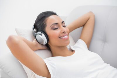 Cute smiling woman lying on couch while listening to music in bright living room
