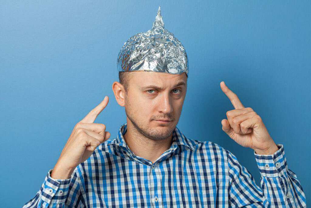 Man with a serious face shows a finger at a cap with aluminum foil.