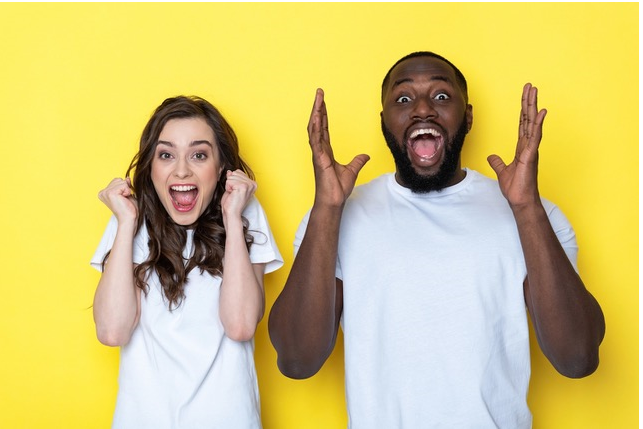 A man and woman standing side-by-side, with excited expressions, against a yellow background.