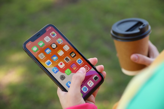 Woman's hands holding and iPhone and a cup of coffee outside on a grass lawn. 