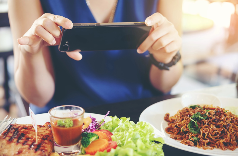 A picture of a woman at a table taking a photo of the meal with her smartphone. 