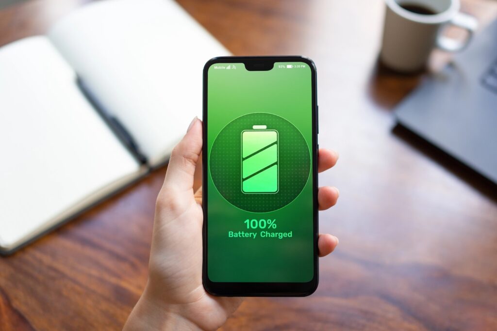 A man's hand holding an iPhone with 100% battery charge.