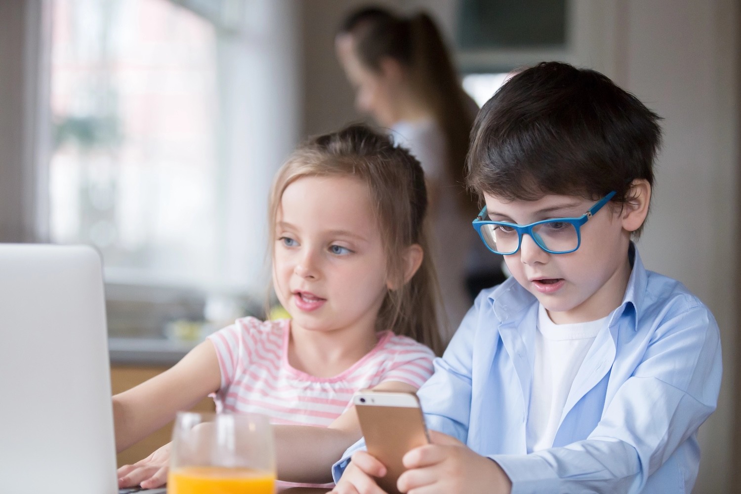 Children playing with a laptop and smartphone while mother is busy. 