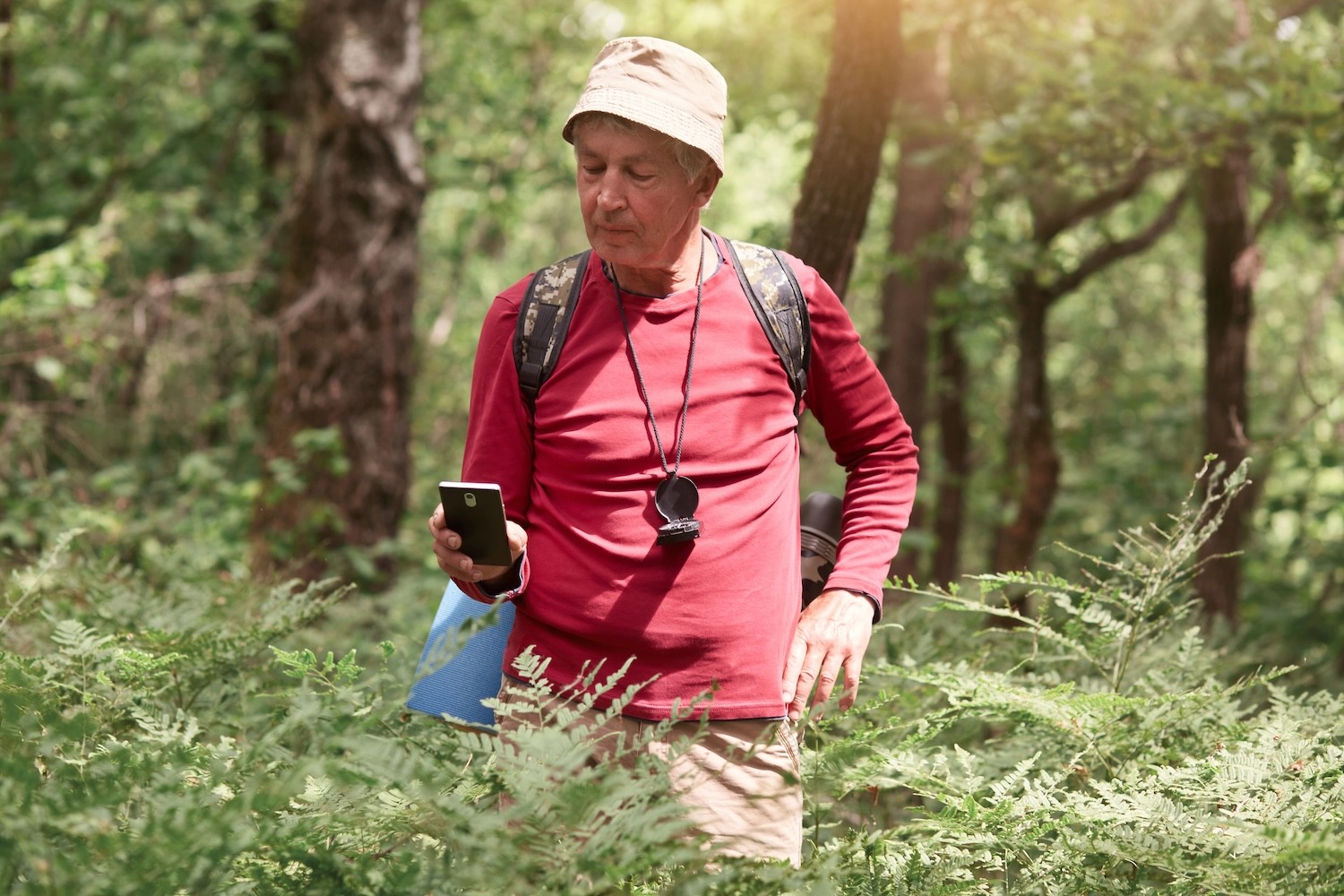 Mature man in forest, standing with mobile phone in hand. 