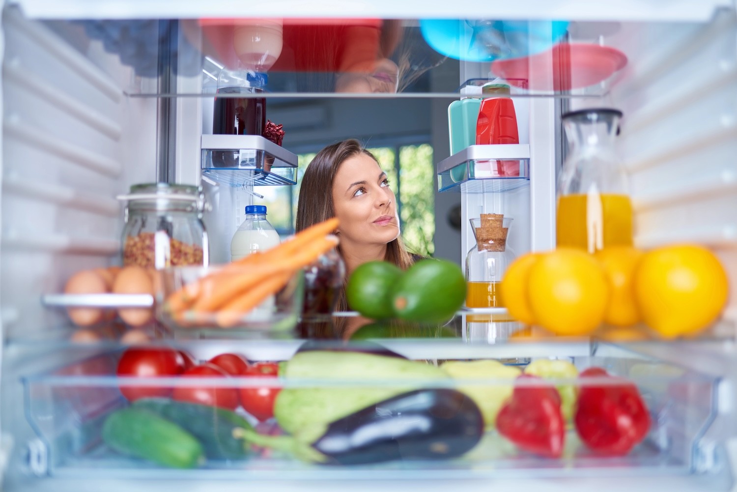 Confused hungry woman standing in front of opened fridge full of groceries.