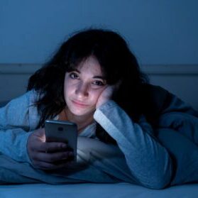 Addicted young woman chatting and surfing on the internet using her smart phone sleepy, bored and tired late at night. Dramatic dark light. In Internet, Mobile addiction and insomnia concept.