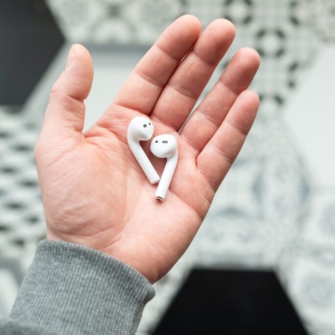 White wireless headphones in a man's hand. The cordless headset lie on the open palm of a male person. Modern mobile technology.