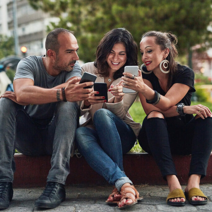 three friends using their cellphones while spending time together in the city
