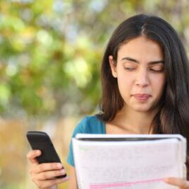 Girl looking sideways at mobile phone while studying in a park with a green background