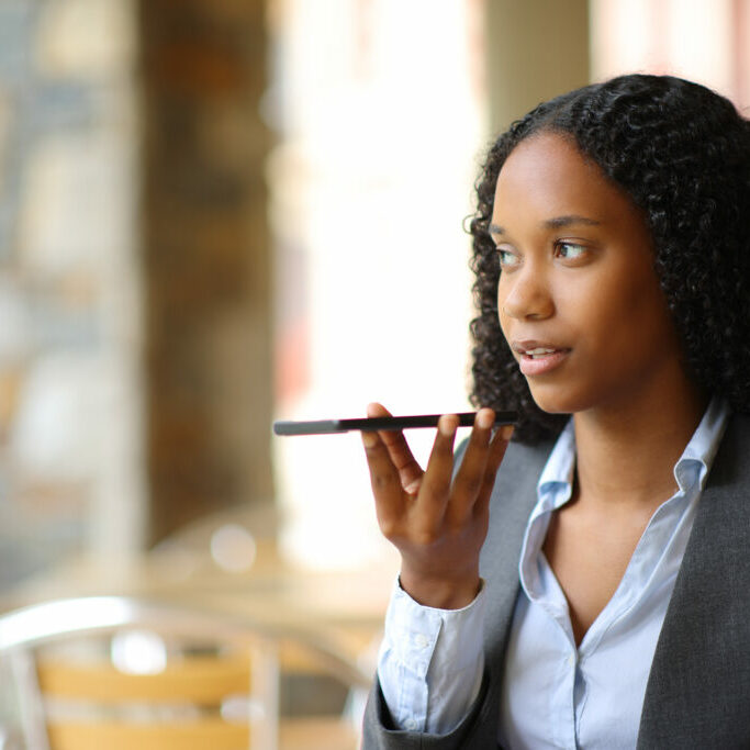 Black businesswoman dictating message on phone in a coffee shop terrace