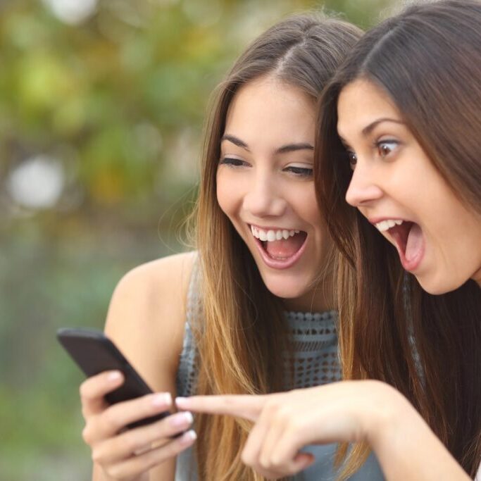 Euphoric friends watching videos on a smartphone and pointing at screen surprised