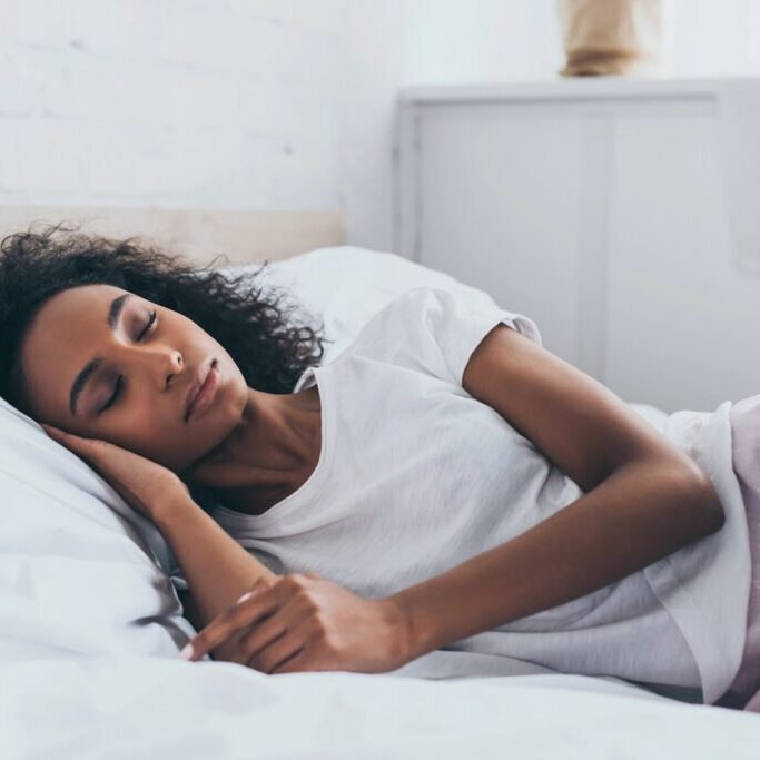 Woman in pajamas sleeping on white sheets.
