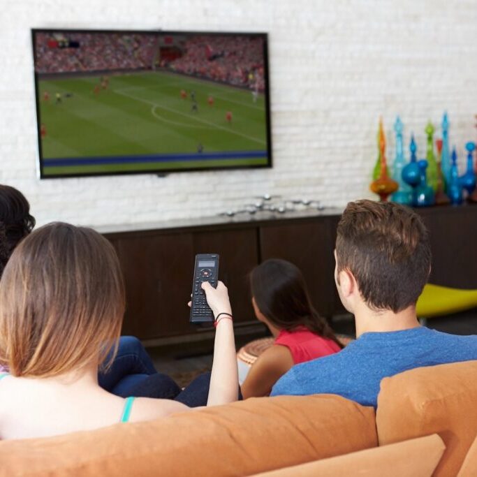 Friends on sofa watching soccer on TV.