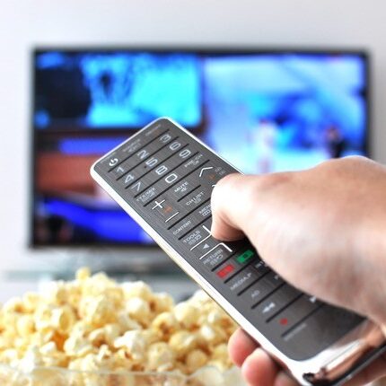 Remote control in hand against popcorn and tv in the background.