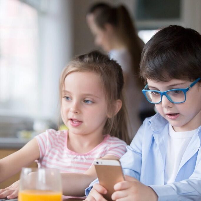 Children playing with a laptop and smartphone while mother is busy.